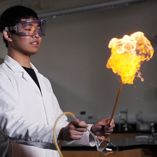 Student creating dramatic flame in chemistry lab experiment. 