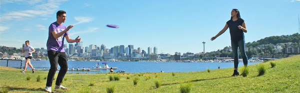 Two students play frisbee at Gas Works Park with South Lake Union in downtown Seattle in the background.