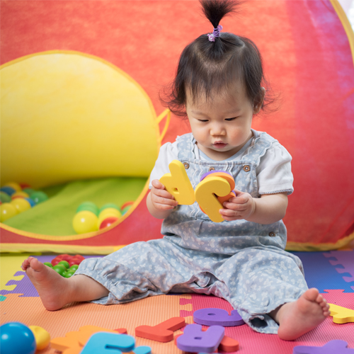 A baby holds brightly colored toys in the shape of letters.