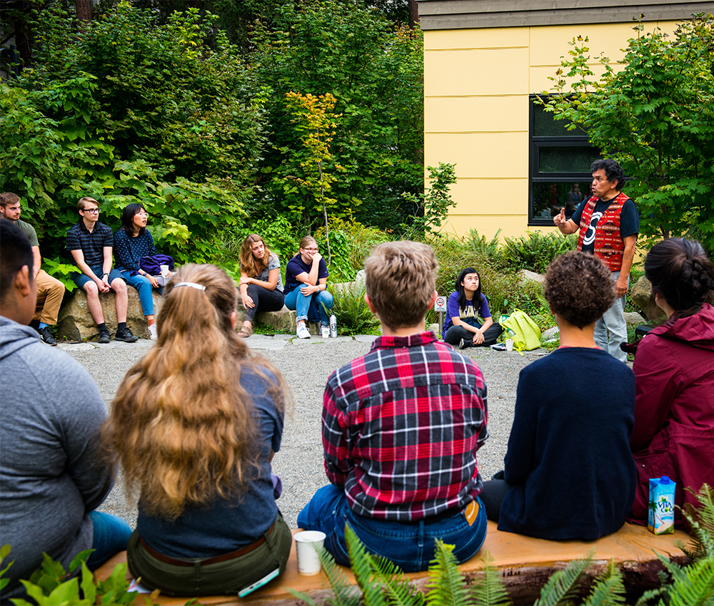 Roger Fernandes (AIS lecturer) telling stories at an AIS Dawg Daze Storytelling event in Autumn 2019 at the gathering circle outside of the Intellectual house.