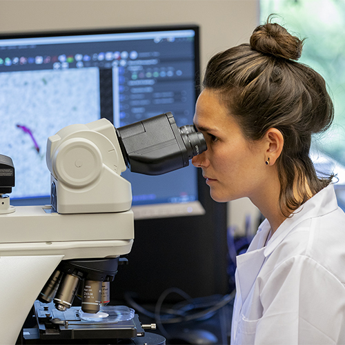 Woman in white lab coat looking into microscope