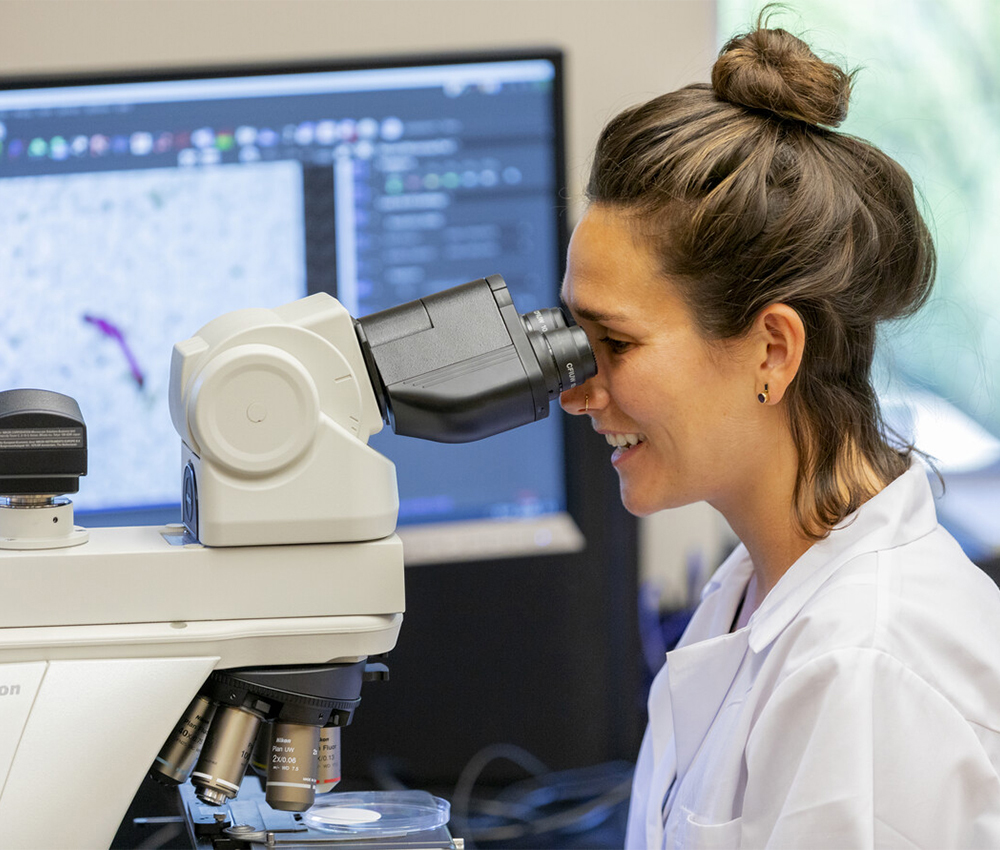 Female student in lab coat looking at microscope