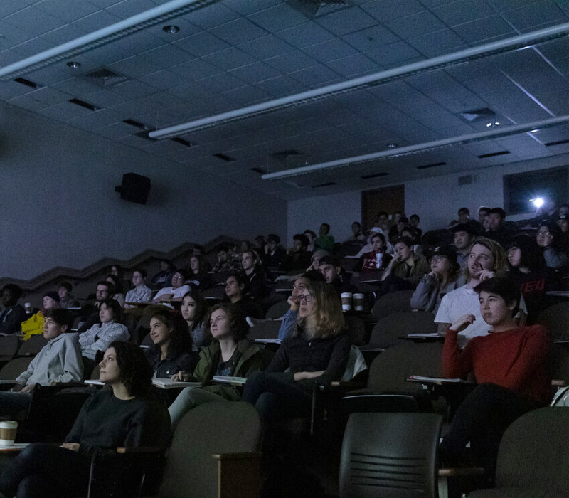 Students in darkened lecture hall looking with projection