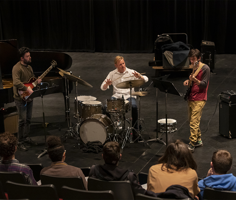 Teacher on drum set with two students playing guitar