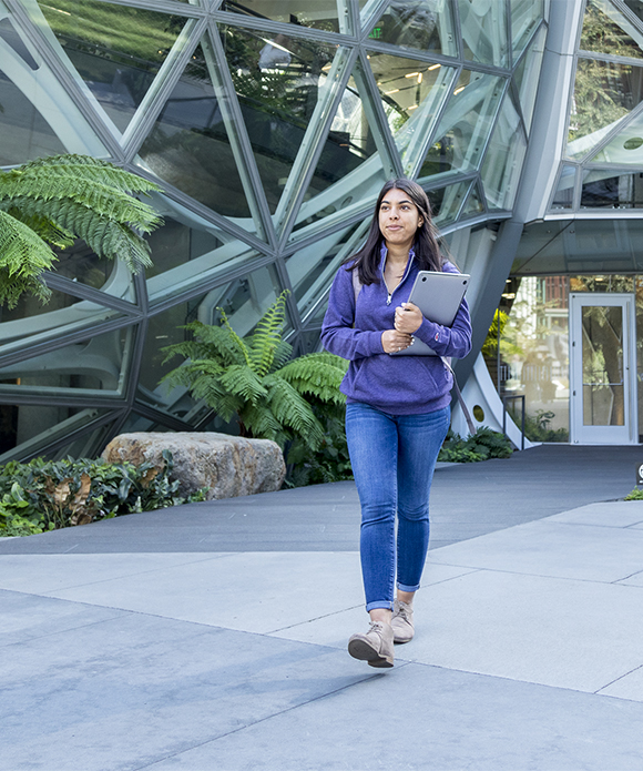 Female student walking with laptop in front of Amazon spheres