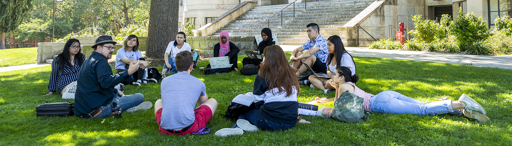 group of students sitting on lawn in circle with teacher