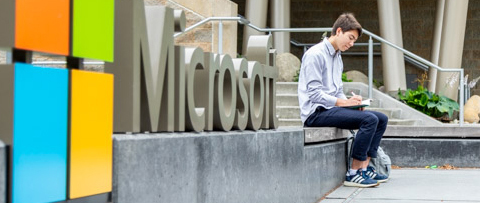 male student sitting in front of microsoft sign