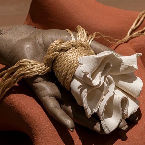 Detail of artwork by Kelly Akash, with dark oversized hand holding tactile object of twine and fabric
